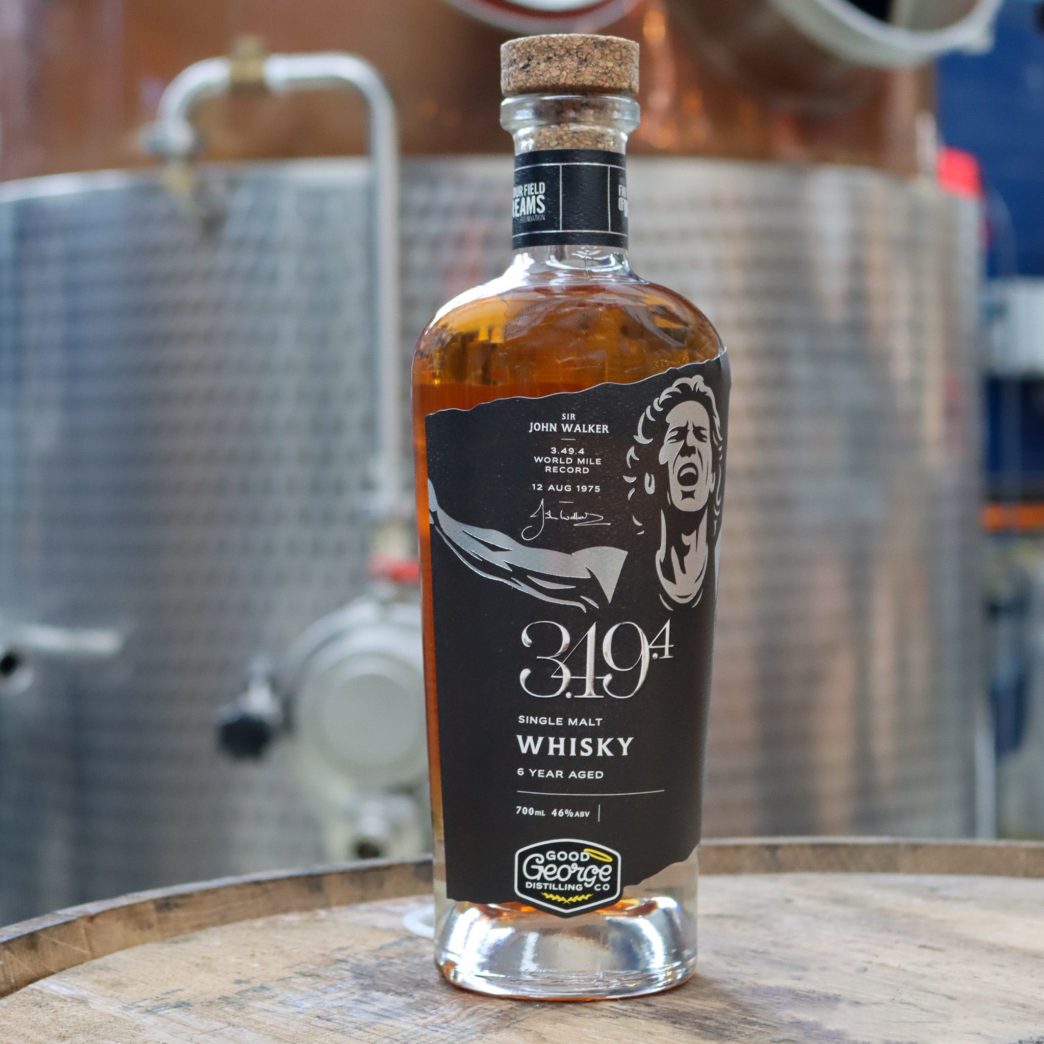 Bottle of 3.49.4 whisky on a wooden barrel with brewing equipment in the background