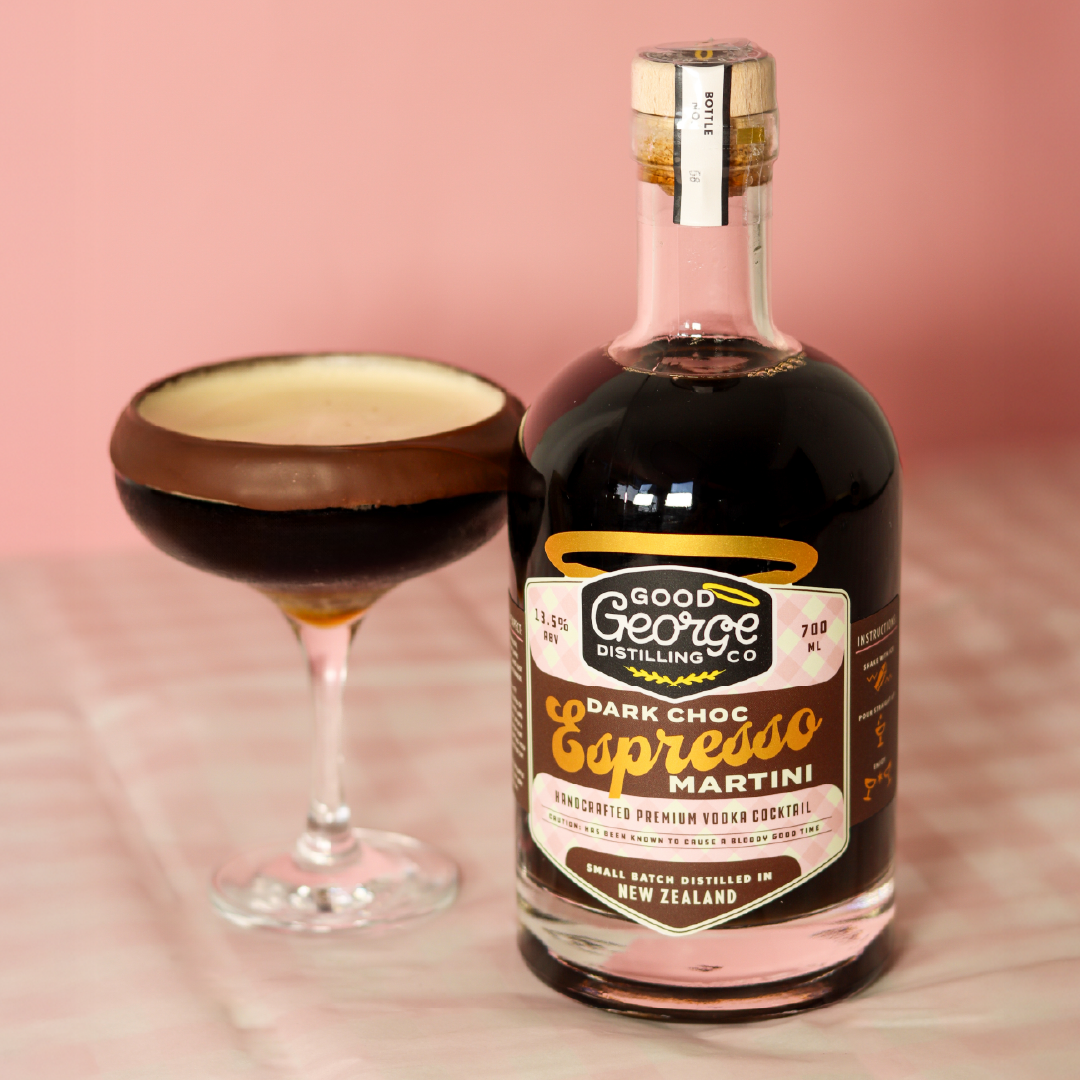 Bottle of Dark Chocolate Espresso Martini with a dark choc martini next to it. Sitting on a pink table cloth and a pink background