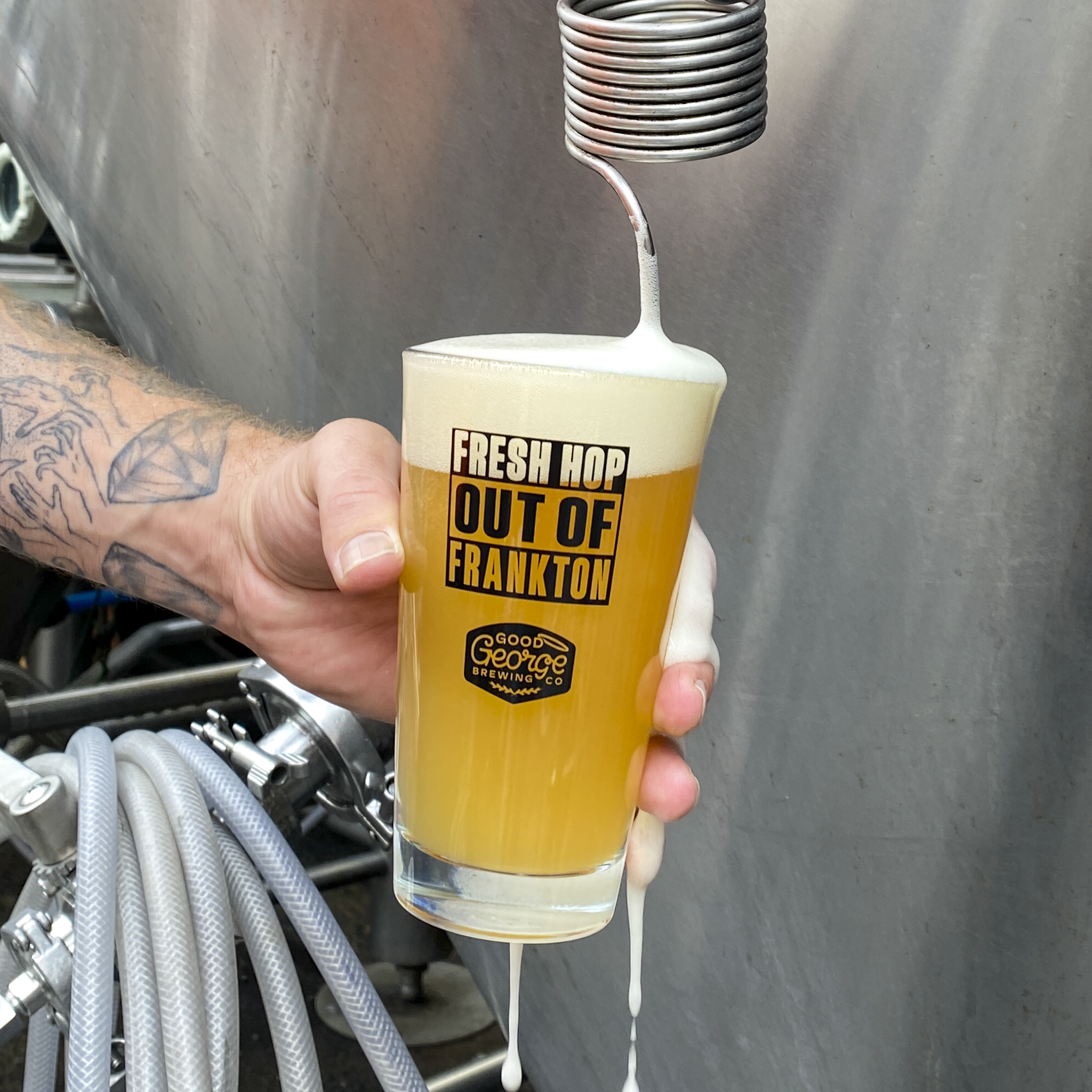Person holding a glass of beer labeled 'Fresh Hop Out of Frankton' with a brewery tap in the background.