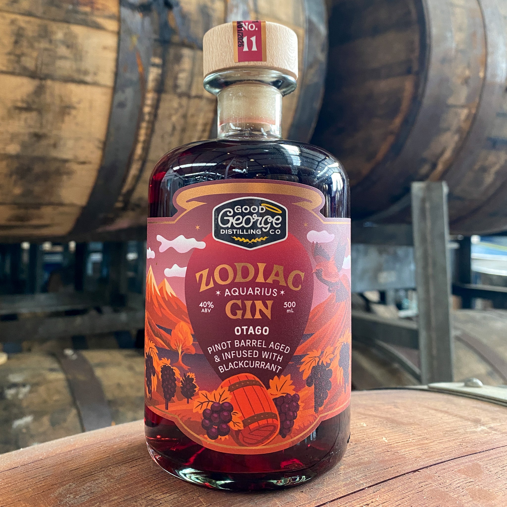 Bottle of Zodiac Gin with a colorful label on a wooden surface, barrels in the background