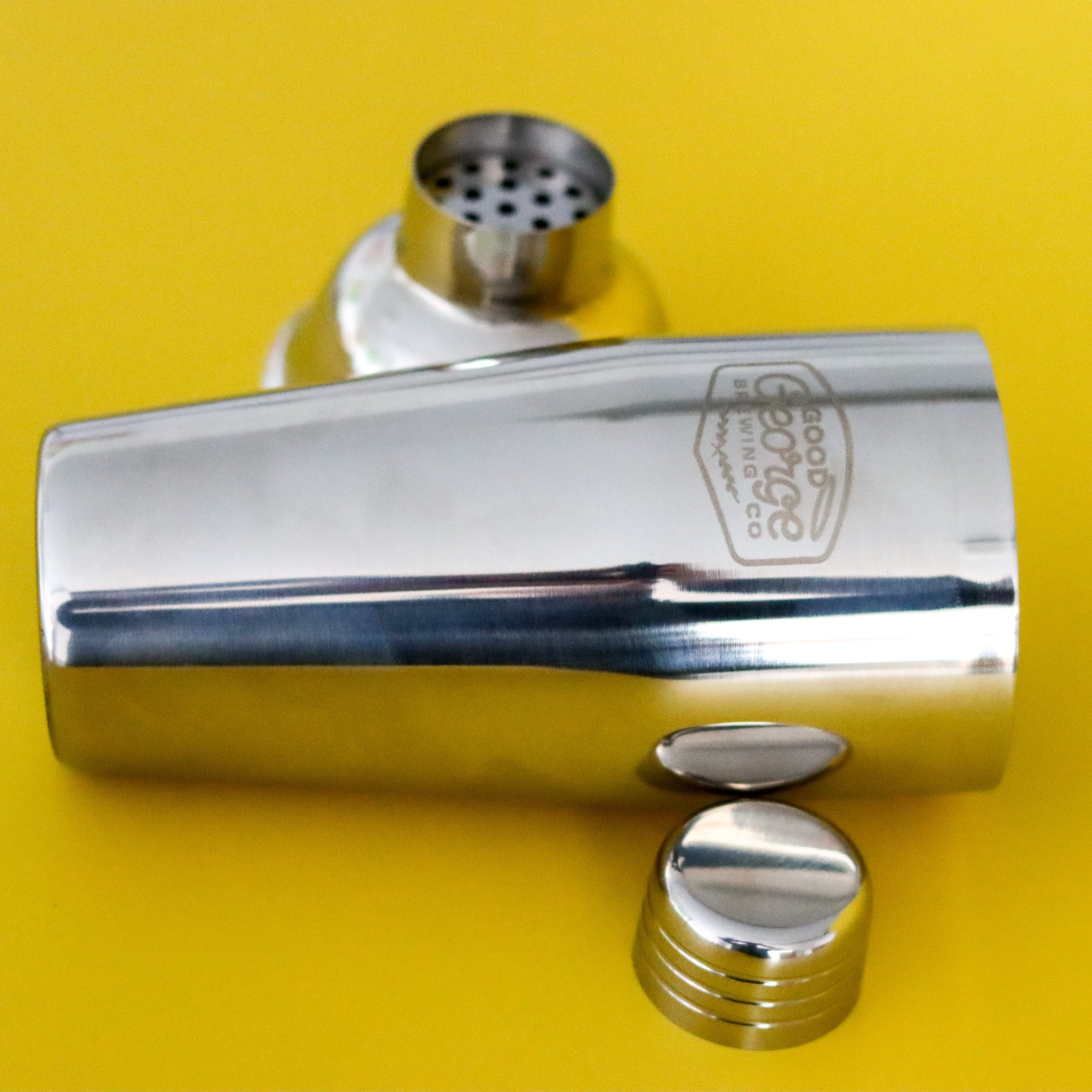 Metallic cocktail shaker with a lid on a yellow background