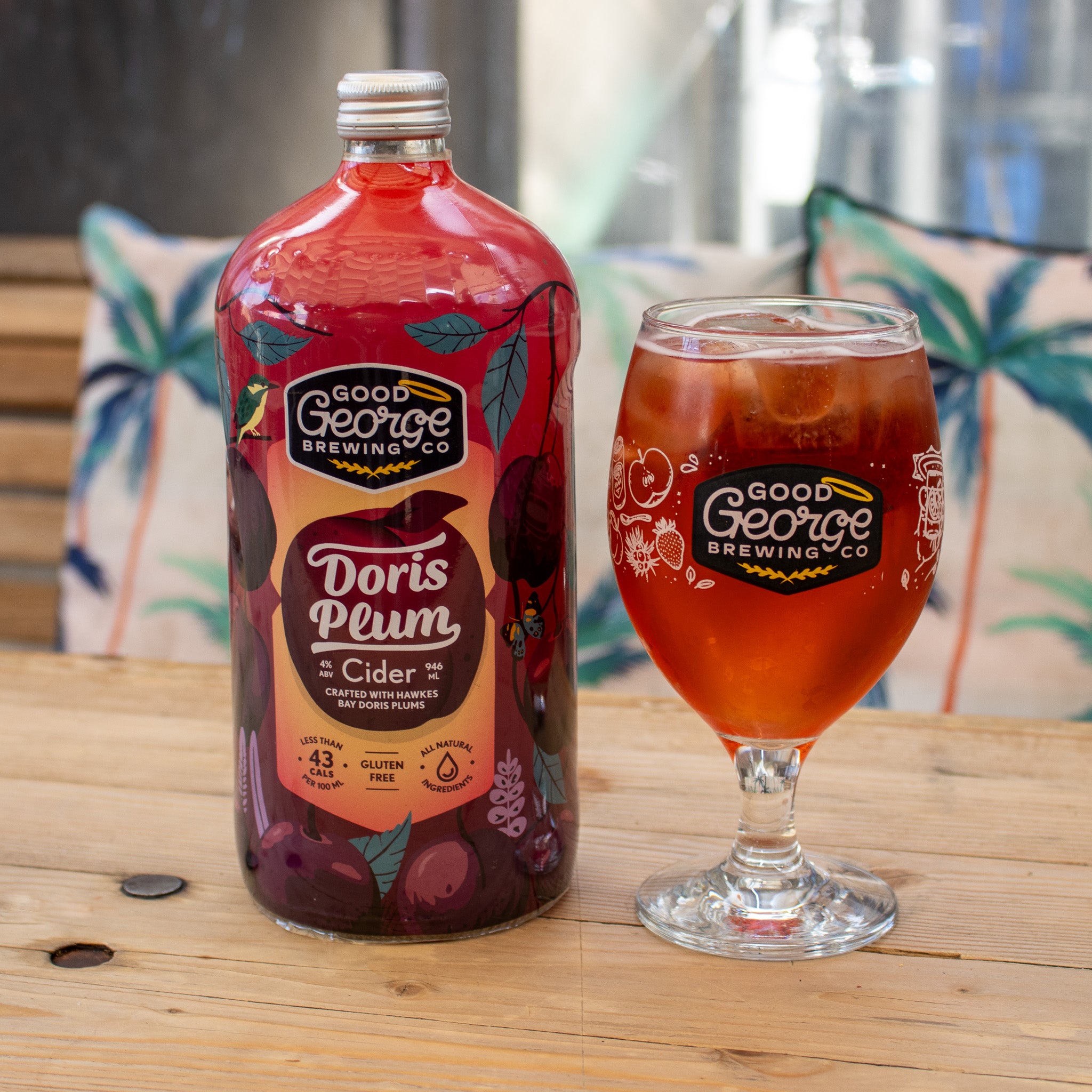 A bottle of Doris Plum Cider with a magenta label a glass of Doris Plum Cider in a glass next to it.