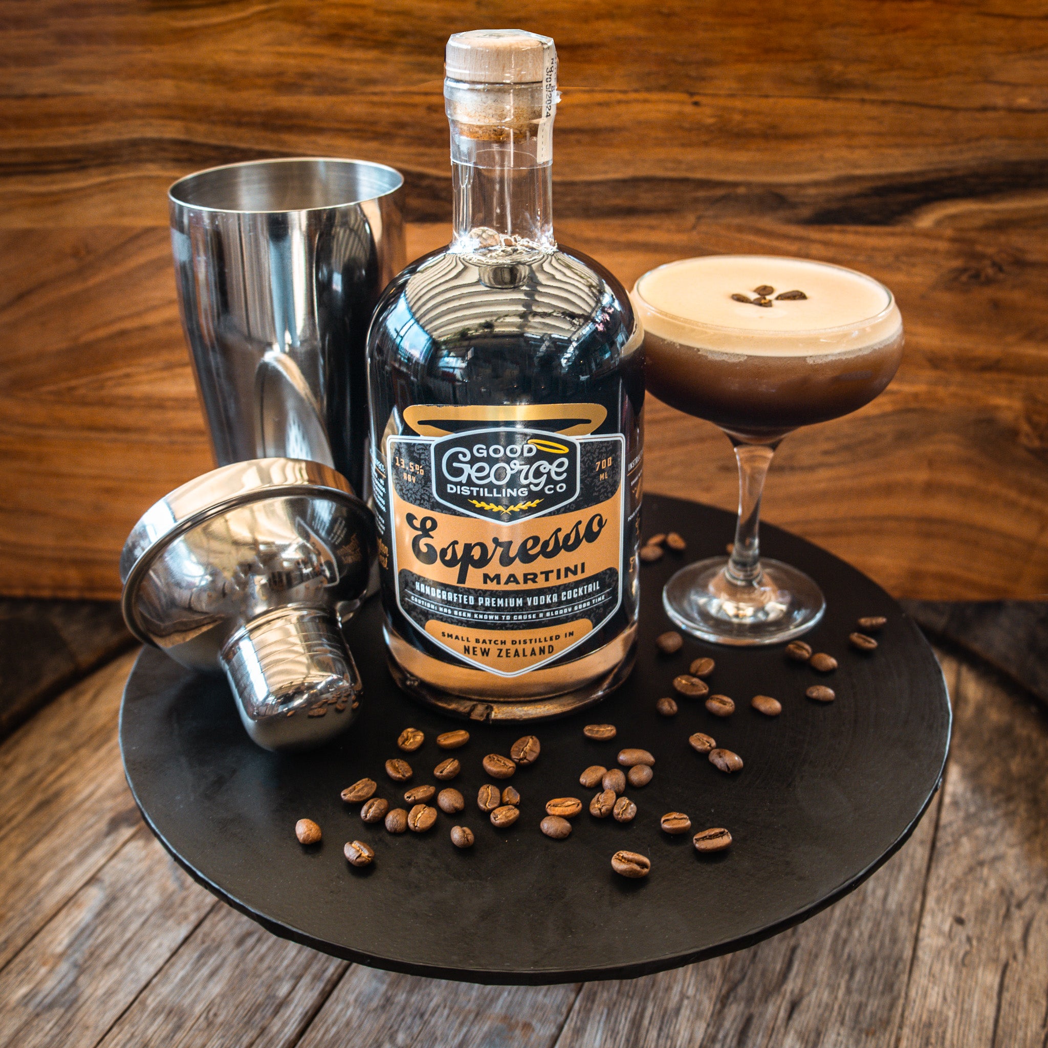 Bottle of Good George Espresso Martini and martini made up with a cocktail shaker and coffee beans surrounding it