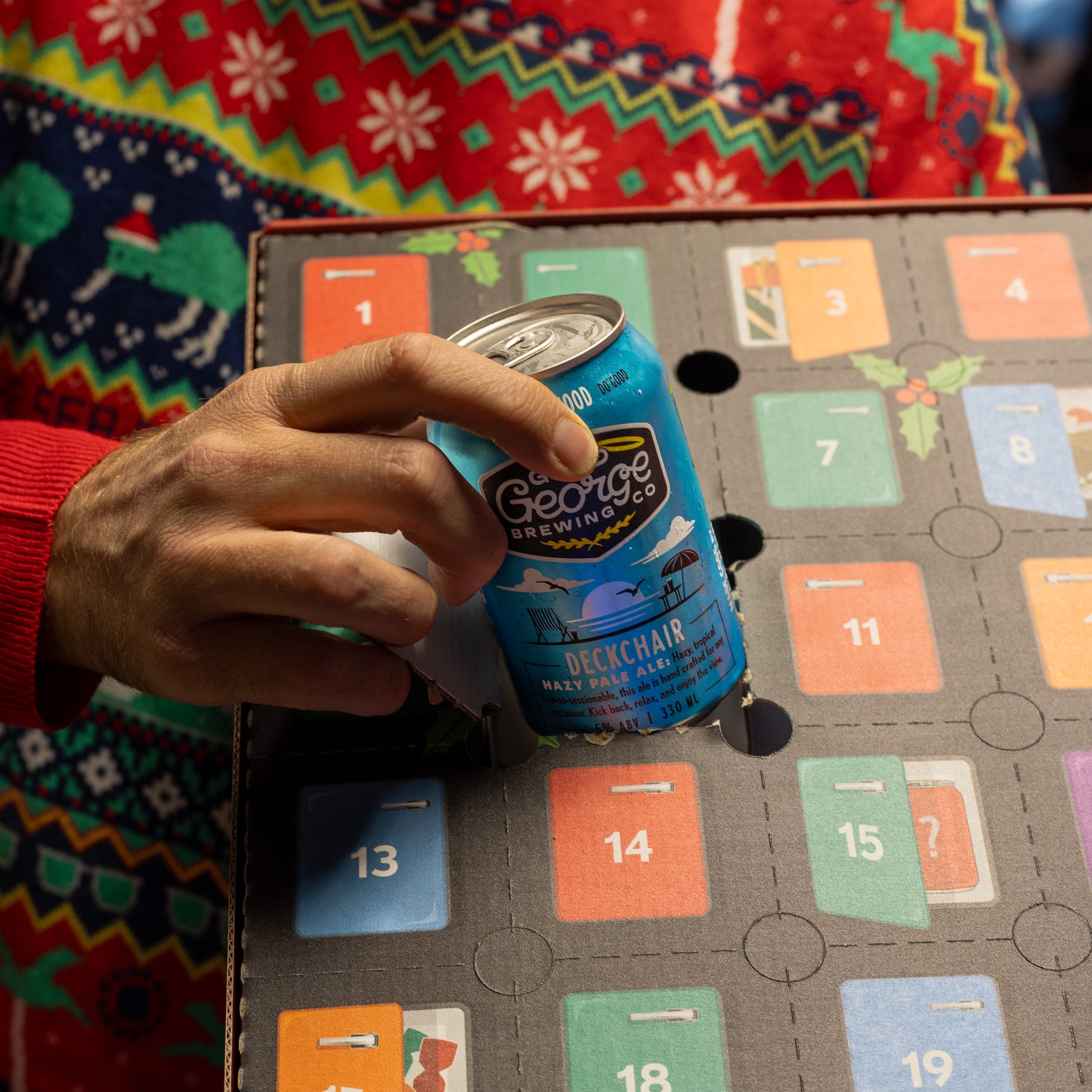 Hand holding a can of George Brewing Co. beer on a festive calendar