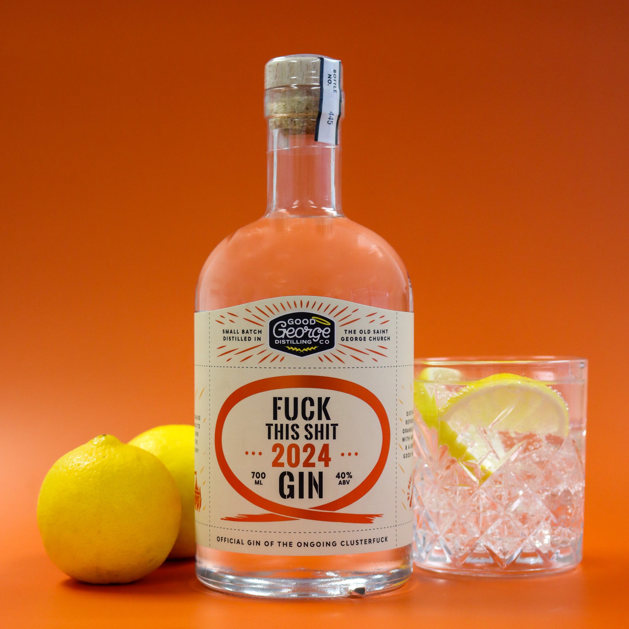 Bottle of gin with a humorous label, lemons, and a glass of gin on an orange background