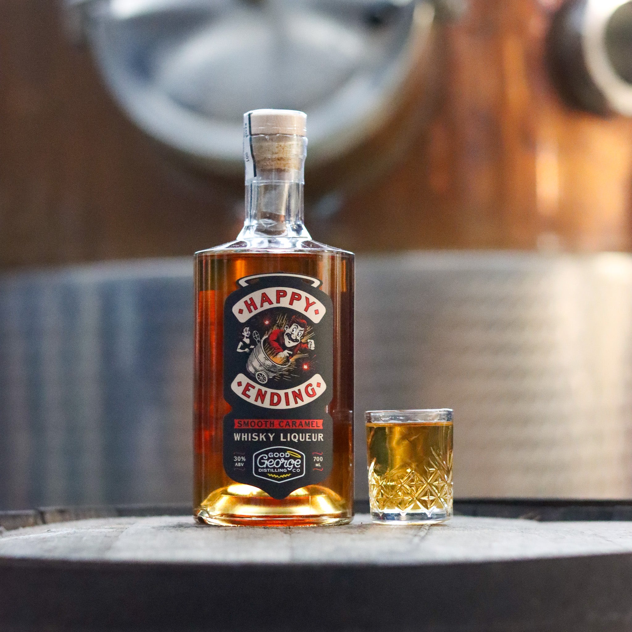 Bottle of 'Happy Endings' whisky liqueur with a glass on a barrel surface.