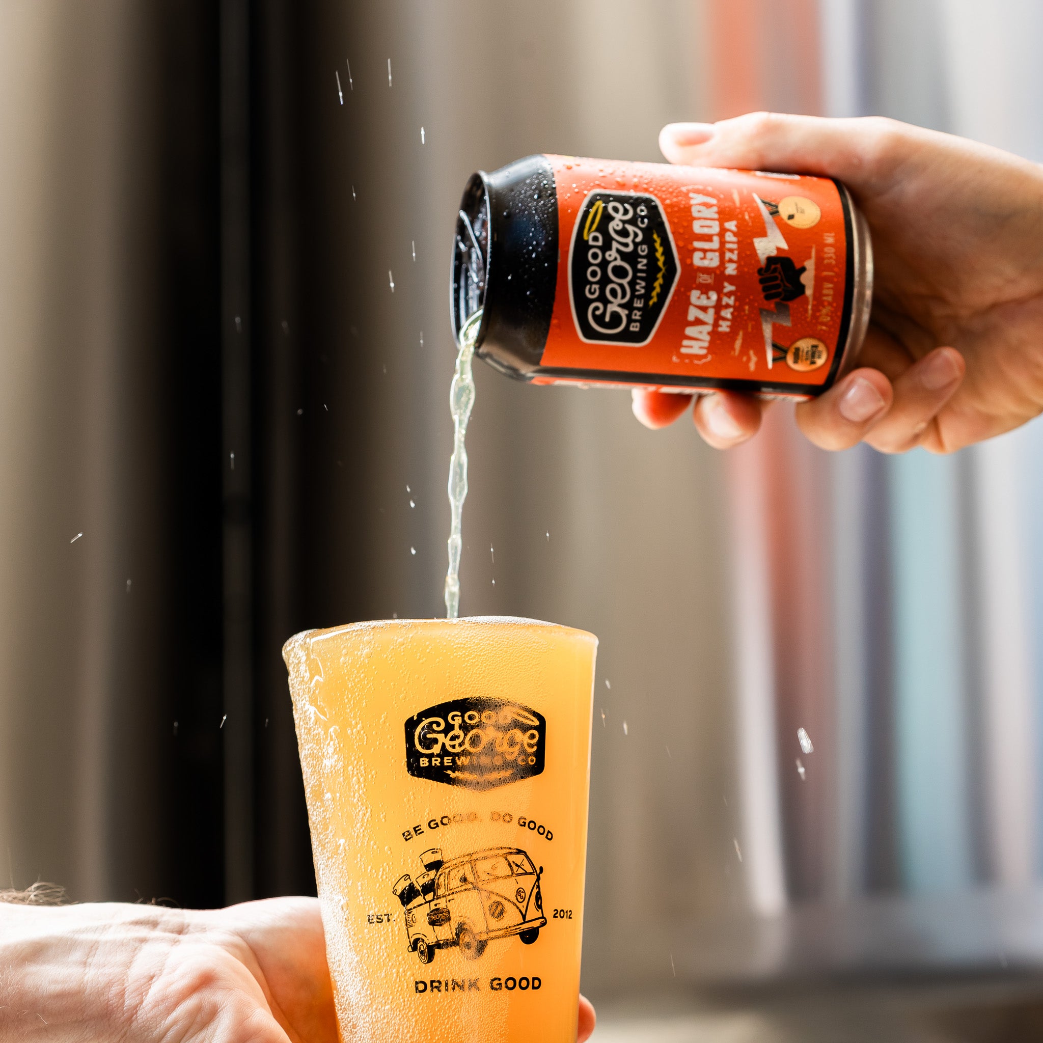 Hand pouring a can of Good George beer into a glass with a blurred background