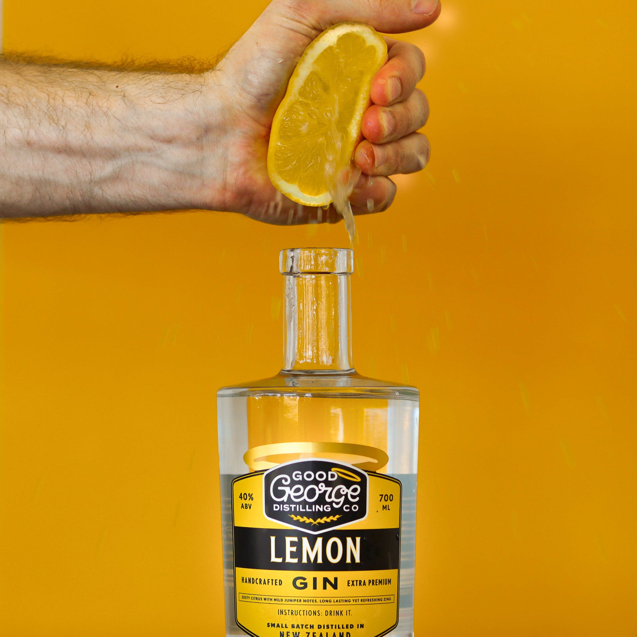 Bottle of Good George Distilling Co Lemon Gin on a yellow background with fresh lemon getting squeezed in