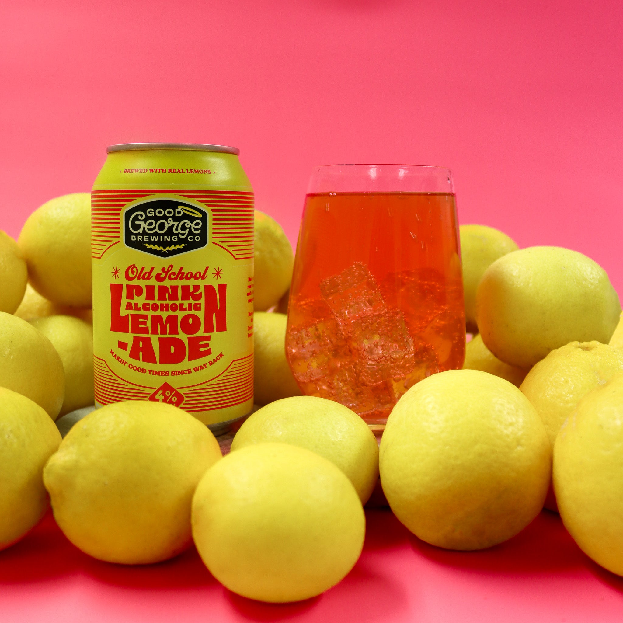 Can of Old School Pink Alcoholic Lemonade with a glass filled with the drink, surrounded by lemons on a pink background.