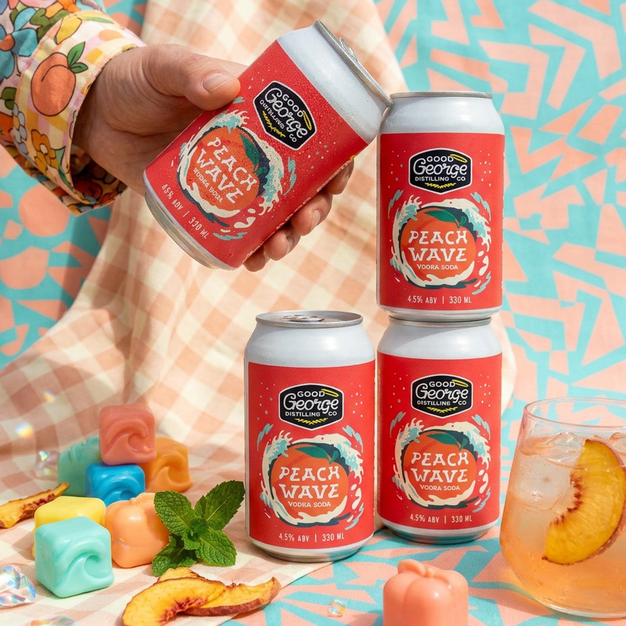 Cans of Peach Wave soda from Good George on a colorful background with peaches and mint.