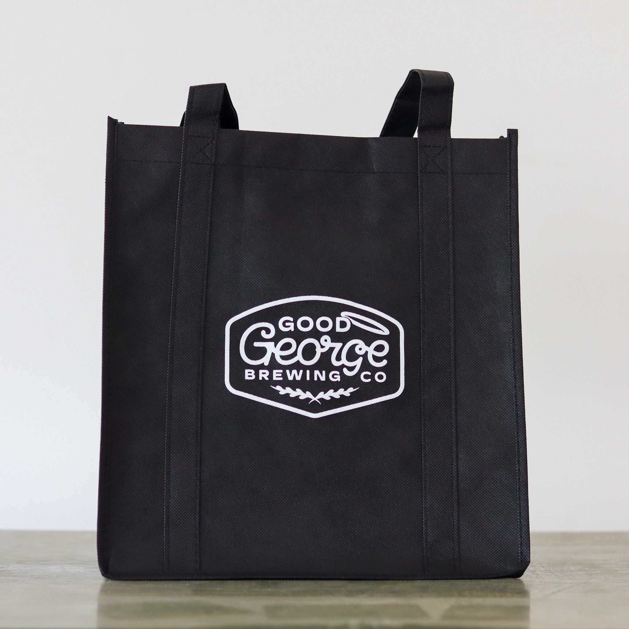 A black Good George tote bag with the brand's logo printed in white.