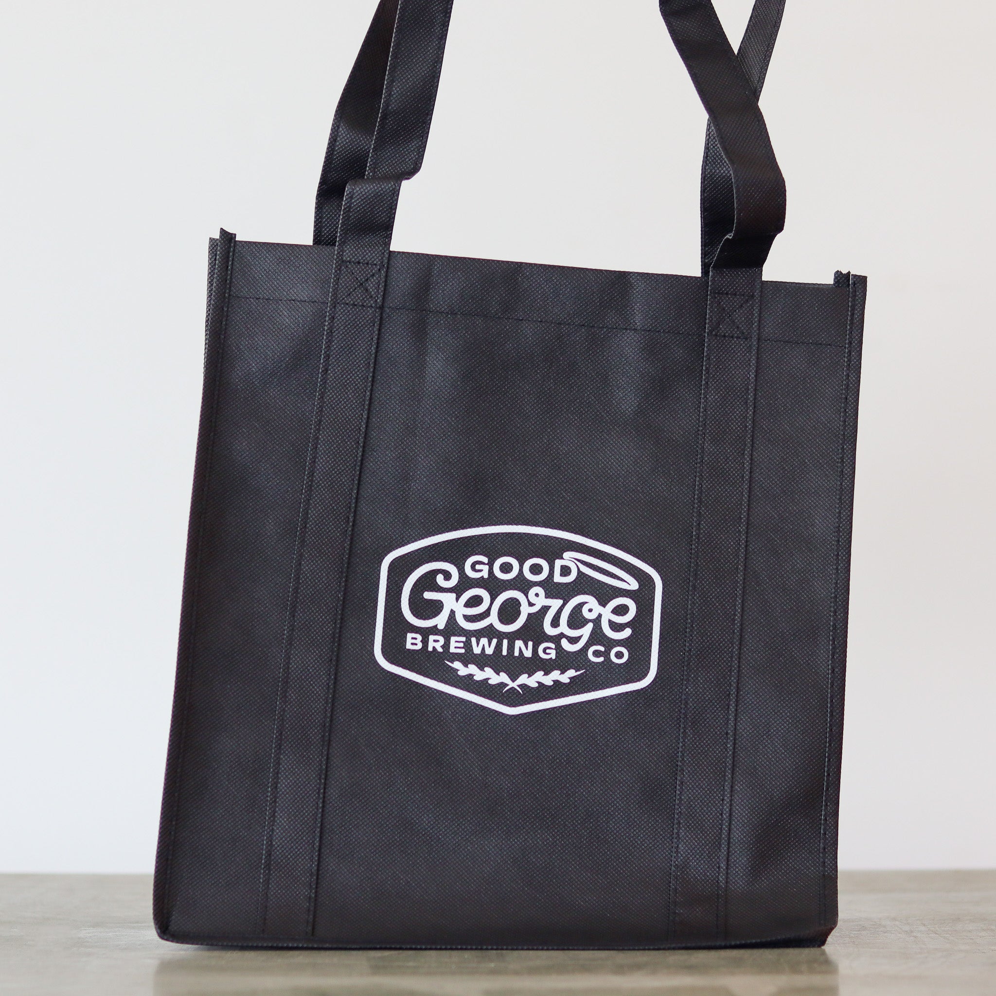 A black Good George tote bag with the brand's logo printed in white.