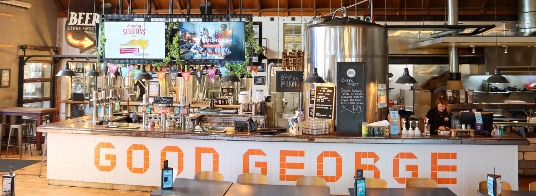 Bar area with 'Good George' branding, bottles on shelves, and a person behind the bar.