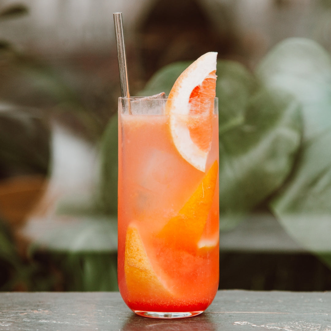 Cocktail with grapefruit slices in a glass on a blurred natural background