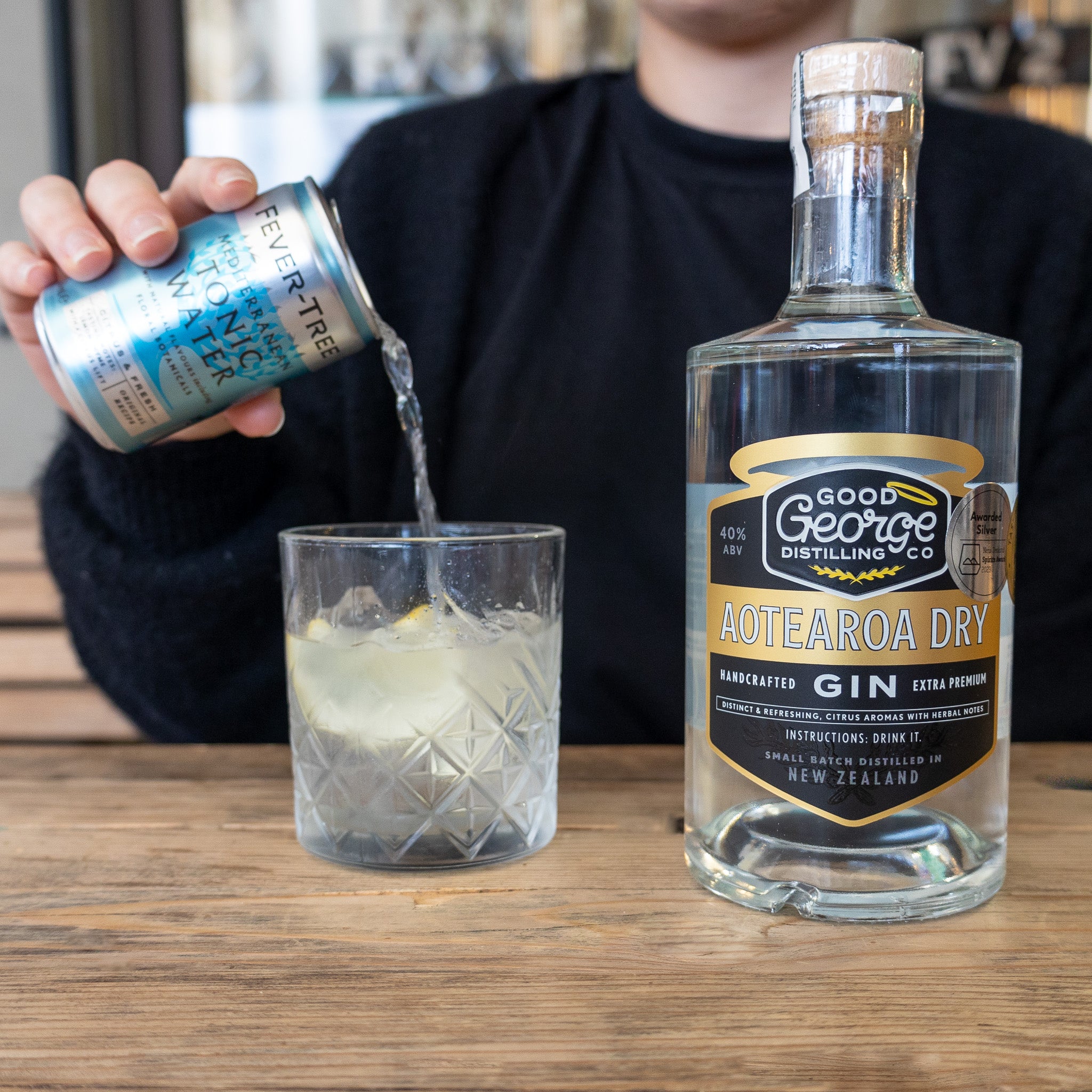 A bottle of Aotearoa Dry Gin by Good George Distilling Co and a gin and tonic getting poured next to it