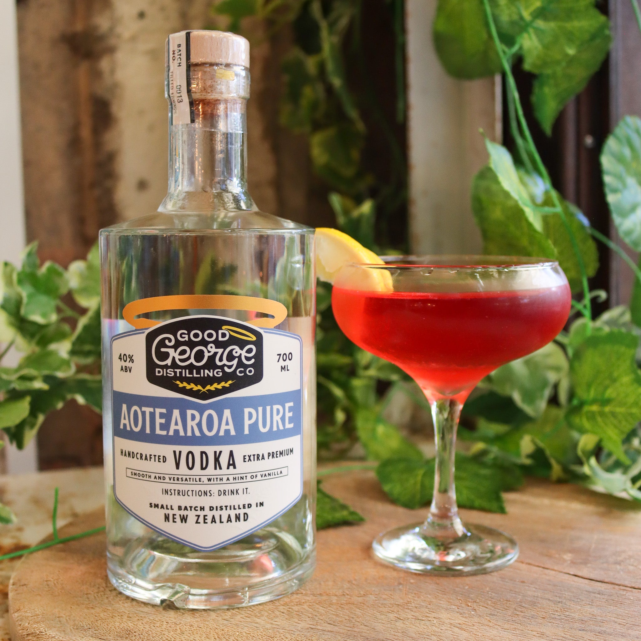 Bottle of Good George Distilling Co. Aotearoa Pure Vodka with a cocktail on a wooden surface with greenery in the background.