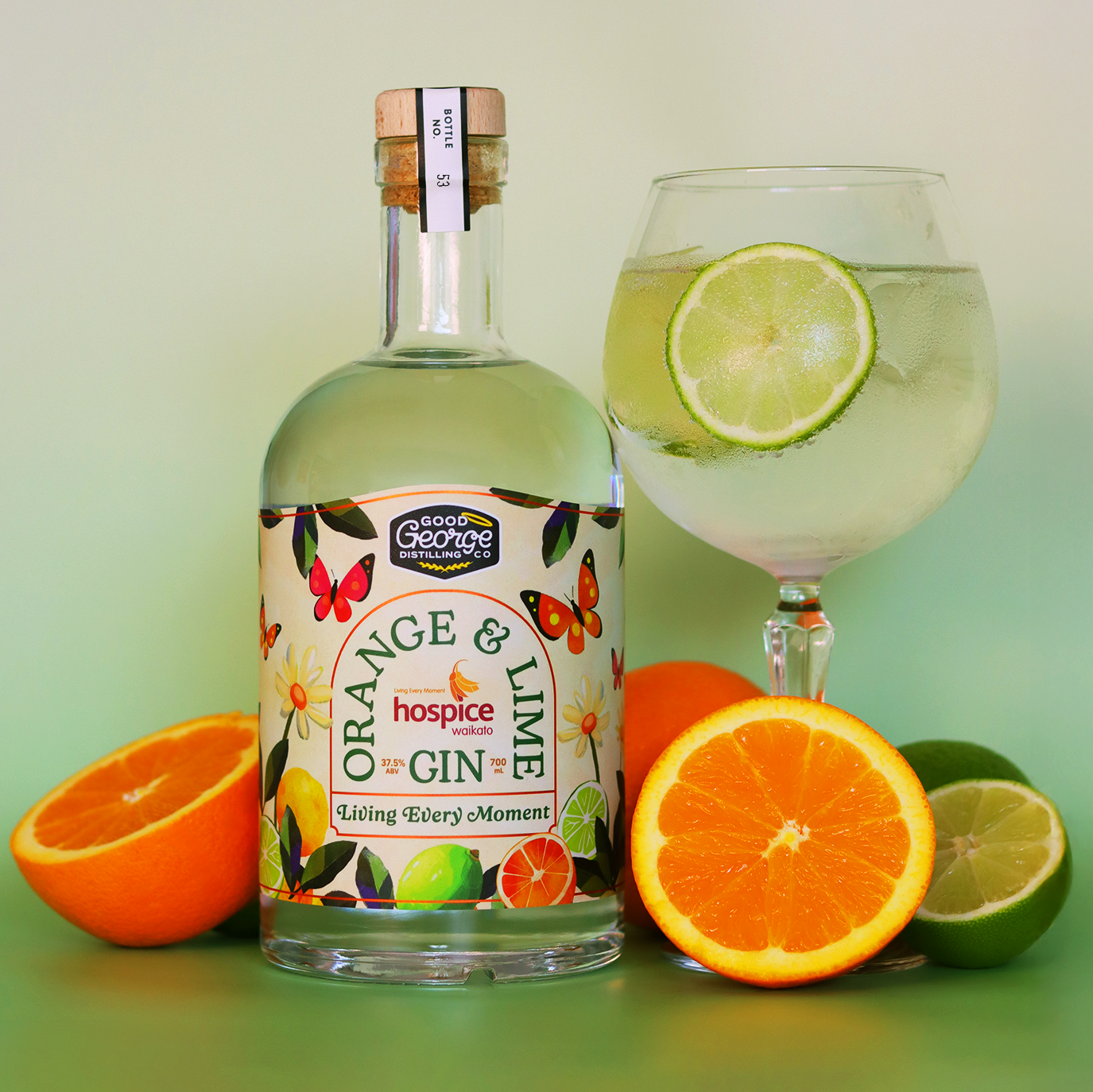 Bottle of orange and lime gin with a glass and citrus fruits on a green background.