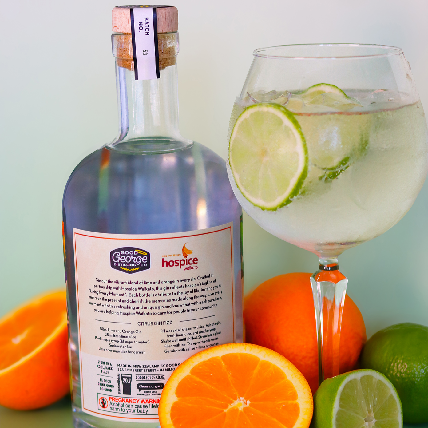 Bottle of gin with a glass of gin and tonic surrounded by citrus fruits on a green surface.