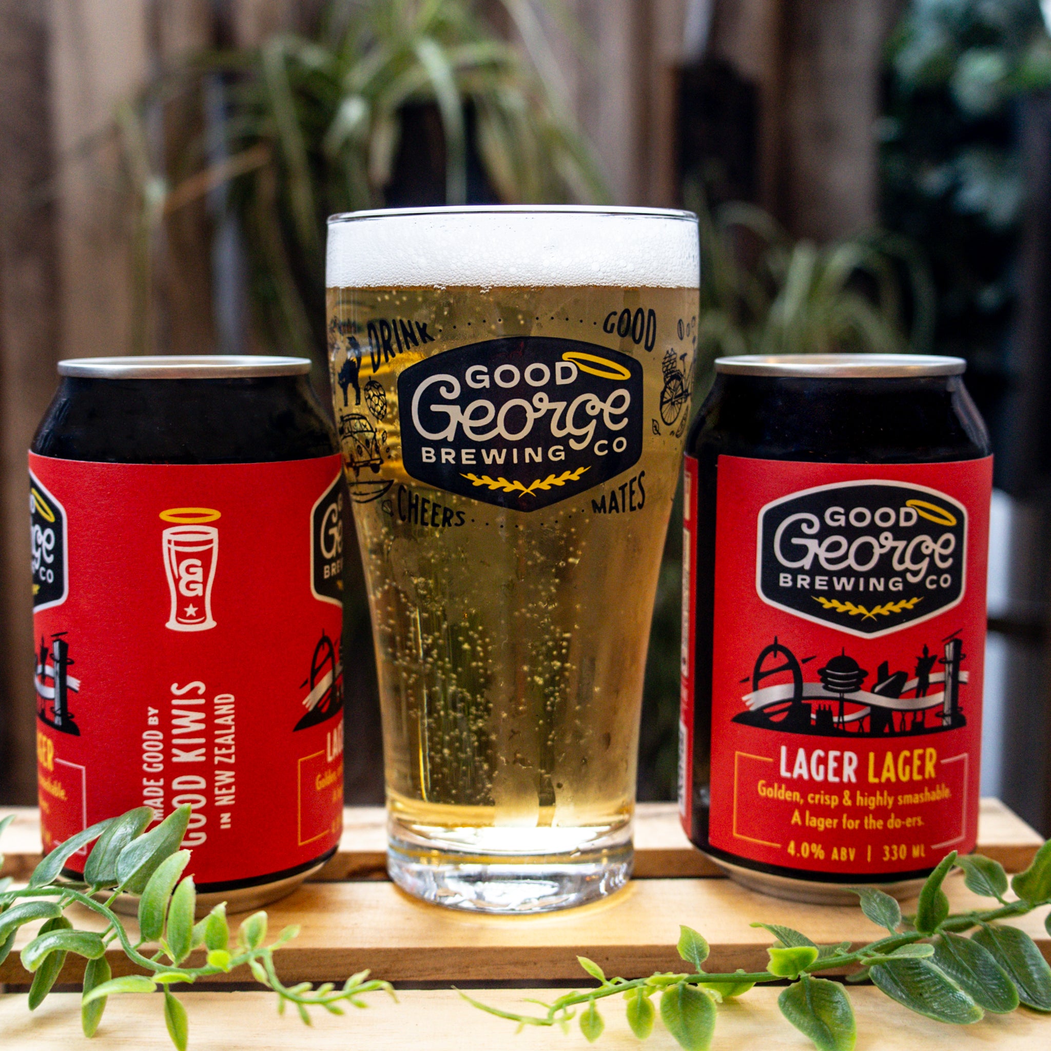 2 Lager Lager cans from Good George Brewing Co, with a beer glass and some greenery