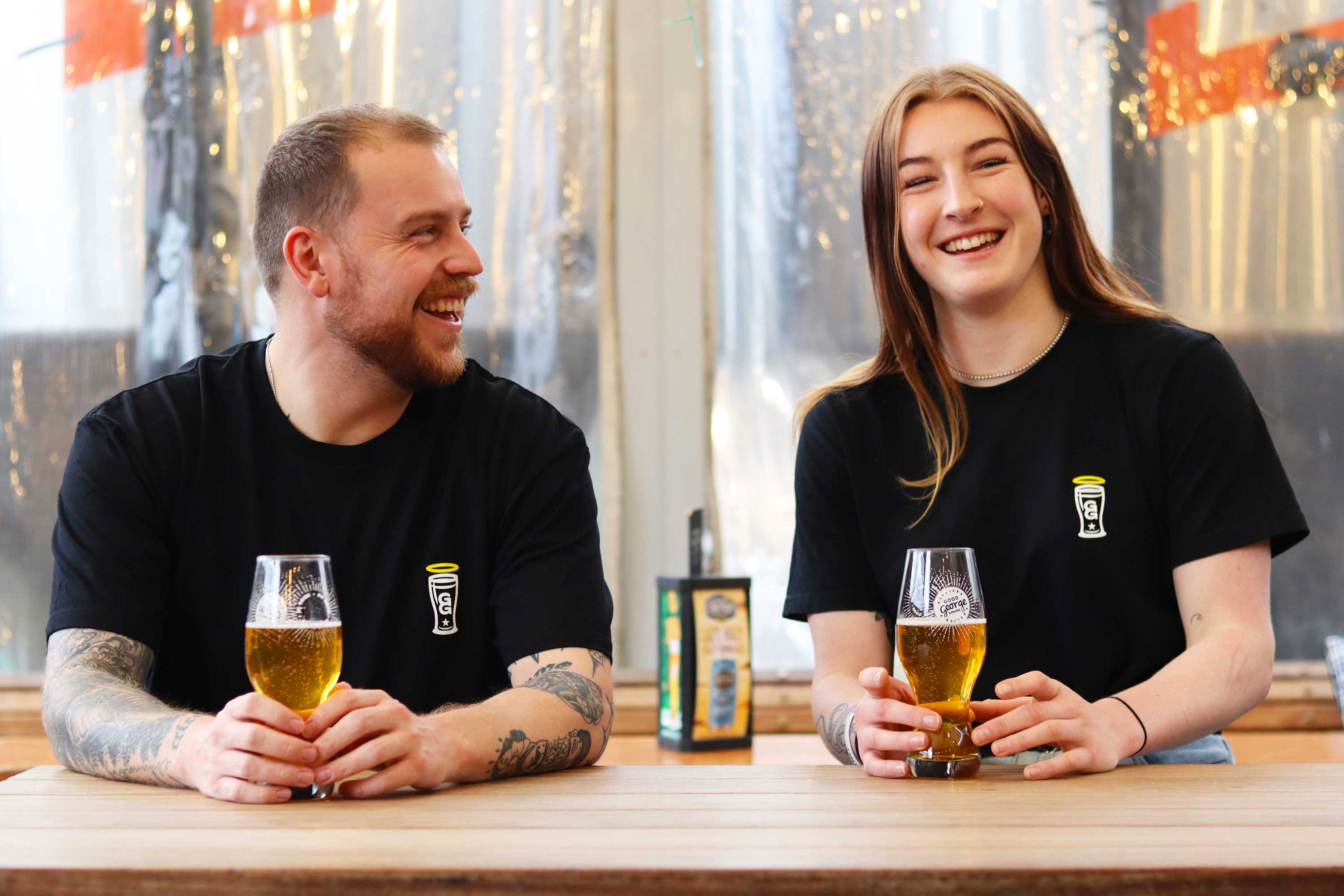 2 people wearing the Black t-shirt with a small graphic at the bar enjoying a beer