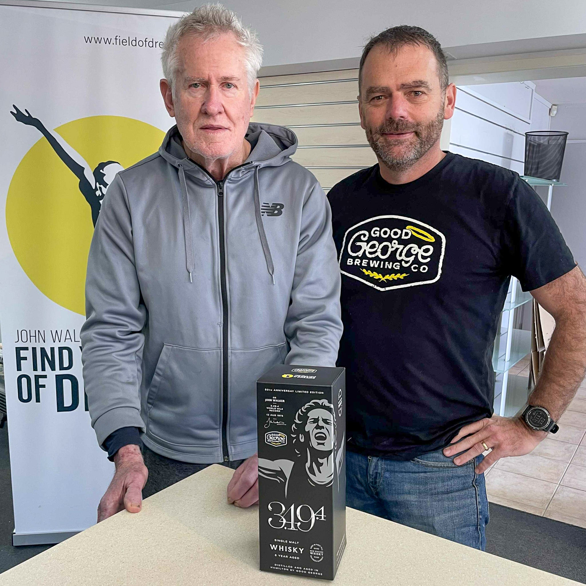 Two men standing behind a whisky box with a visible brand logo in an indoor setting.