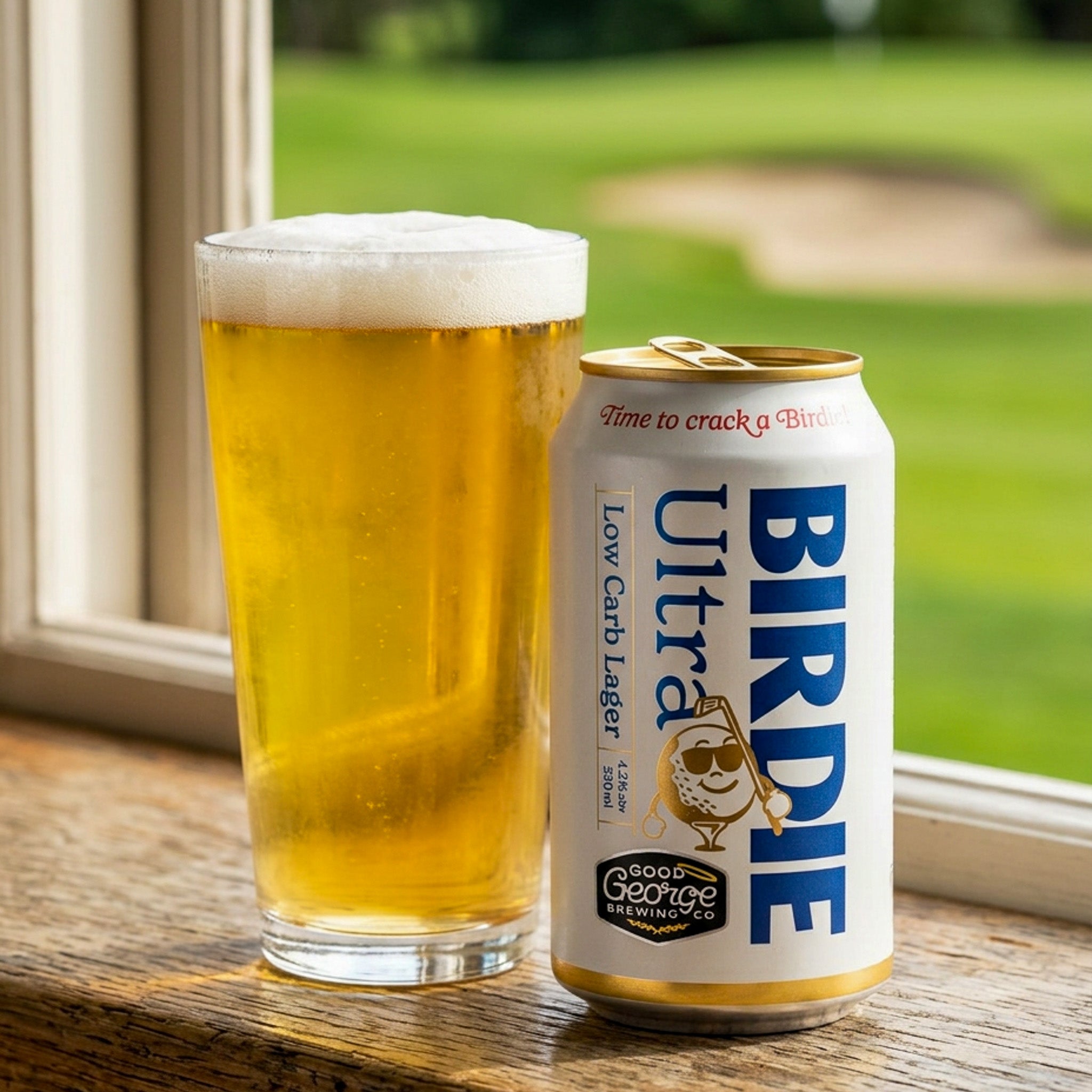 Can of Birdie Ultra Low Carb Lager next to a glass of beer on a wooden surface with a blurred outdoor background.