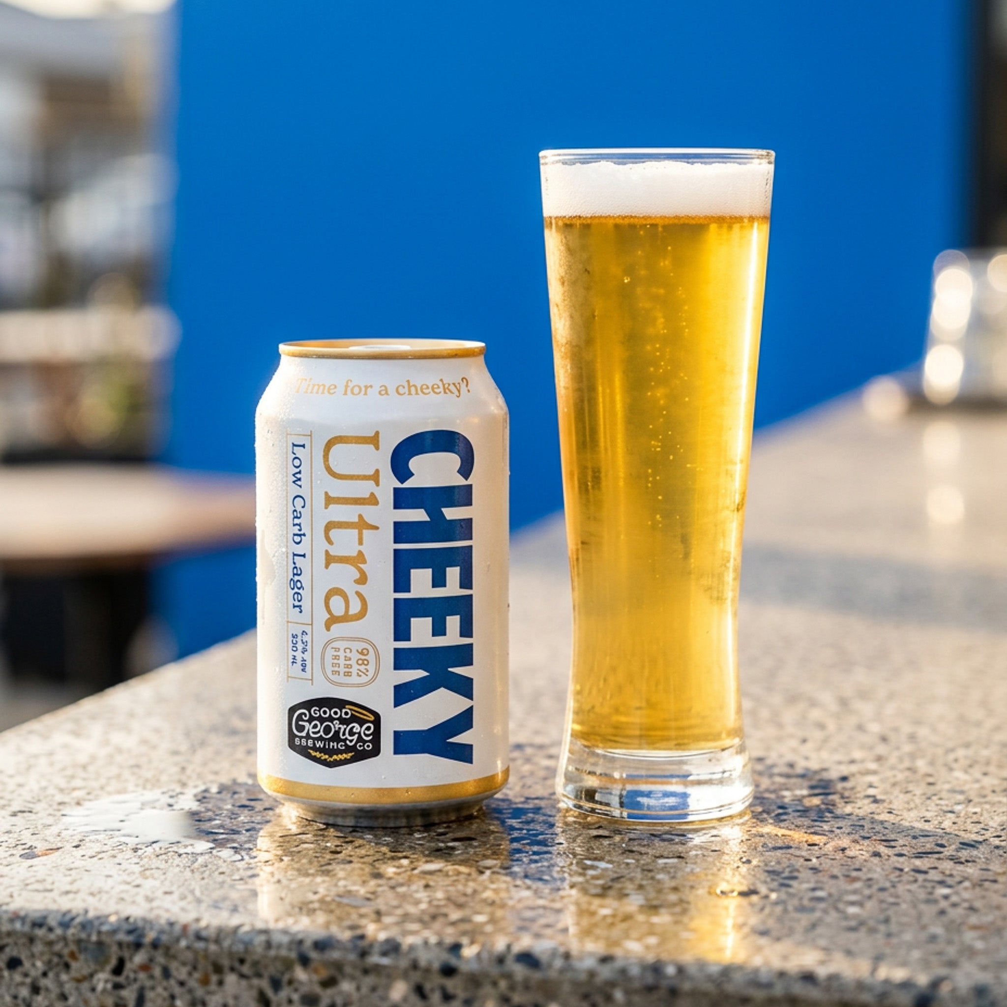 Cheeky Ultra low carb lager can and glass on a table with a blue background
