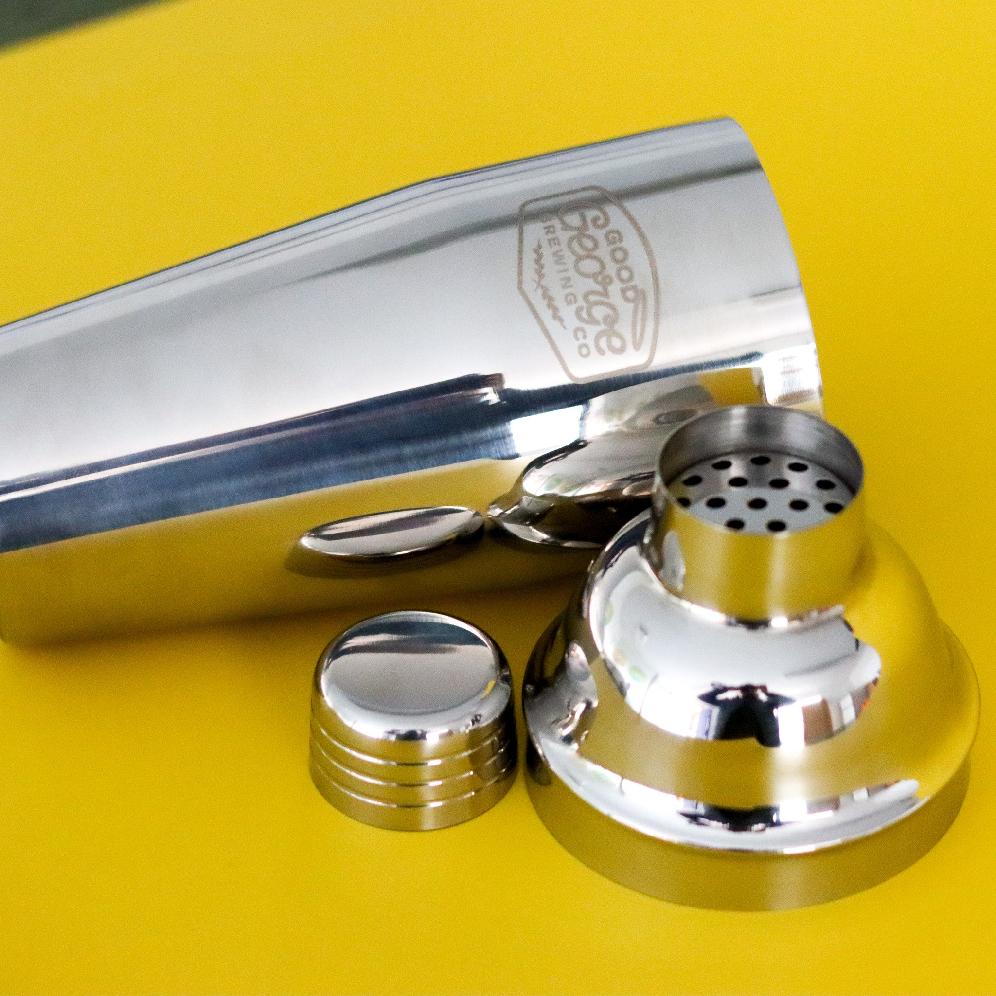 Metallic cocktail shaker with components on a yellow background