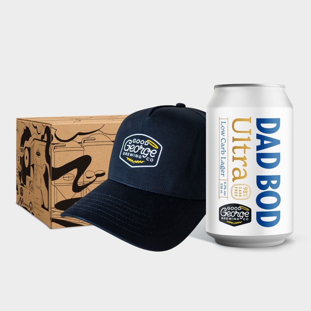A navy blue baseball cap with a 'Good George Brewing Co.' logo, shown next to a white aluminum can labeled 'DAD BOD Ultra' and a brown cardboard gift box with black line art, on a light gray background.