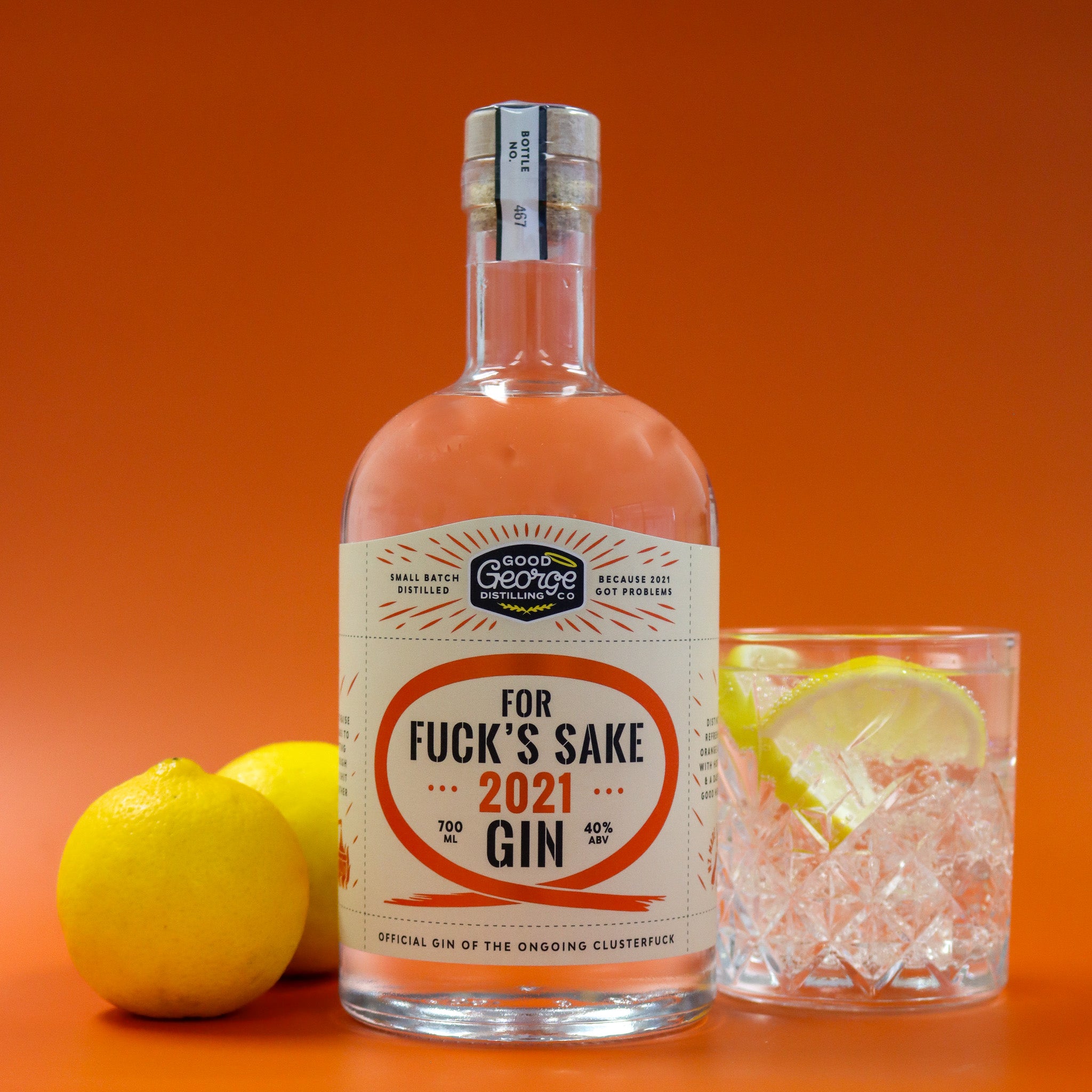 Bottle of 'For Fuck's Sake 2021 Gin' with a glass of gin and lemon on an orange background