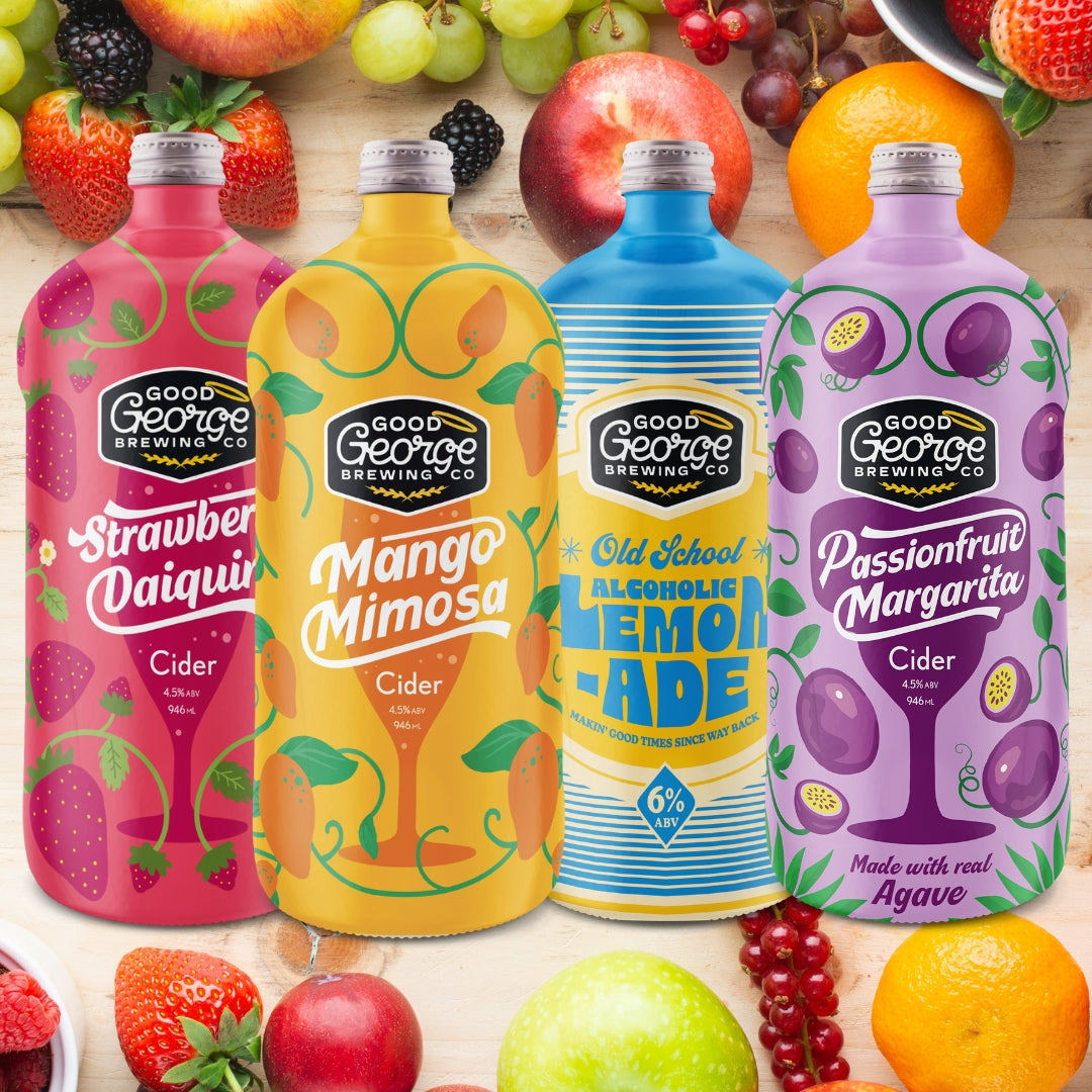 Four colorful bottles of Good George Brewing Co. drinks surrounded by fruits on a wooden surface.