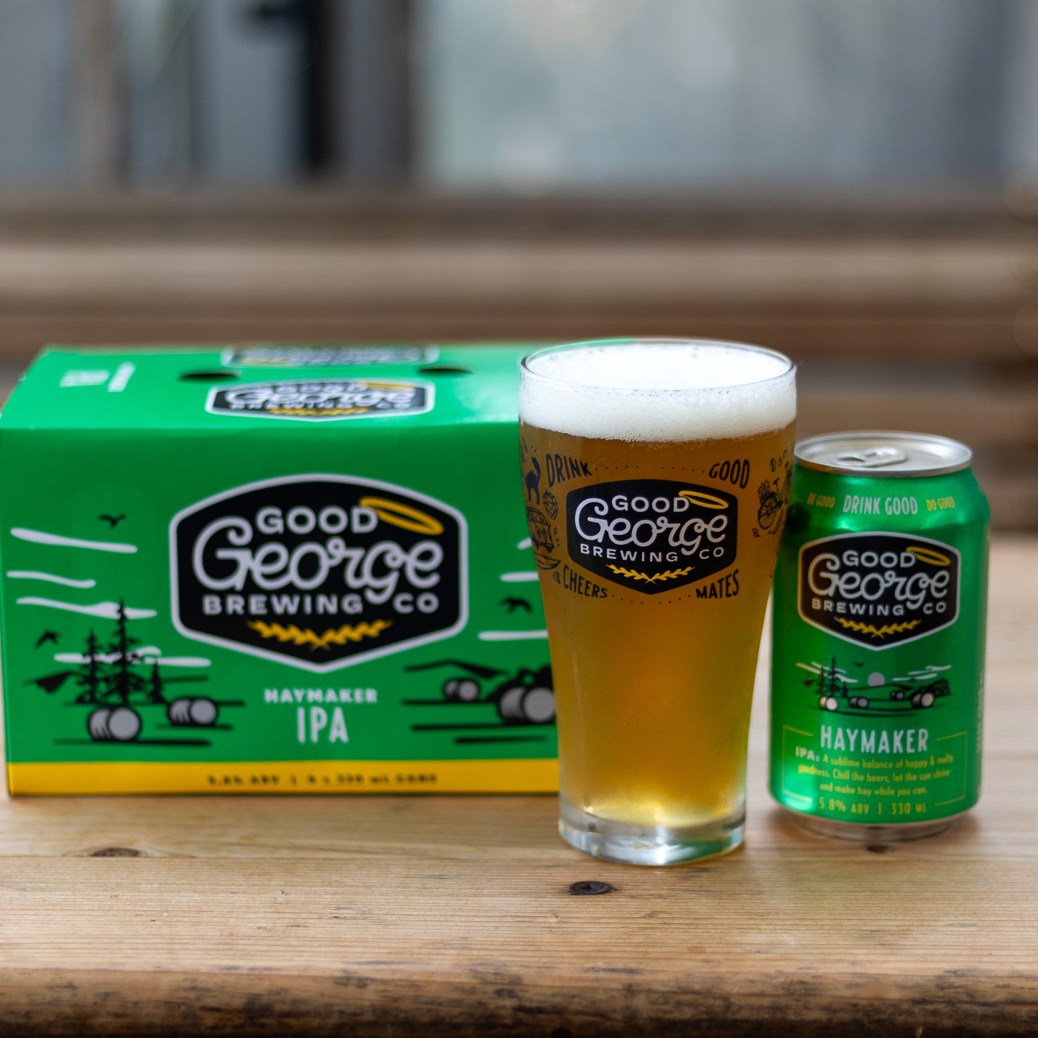 Good George Brewing Co. beer can, glass, and six-pack on a wooden surface.