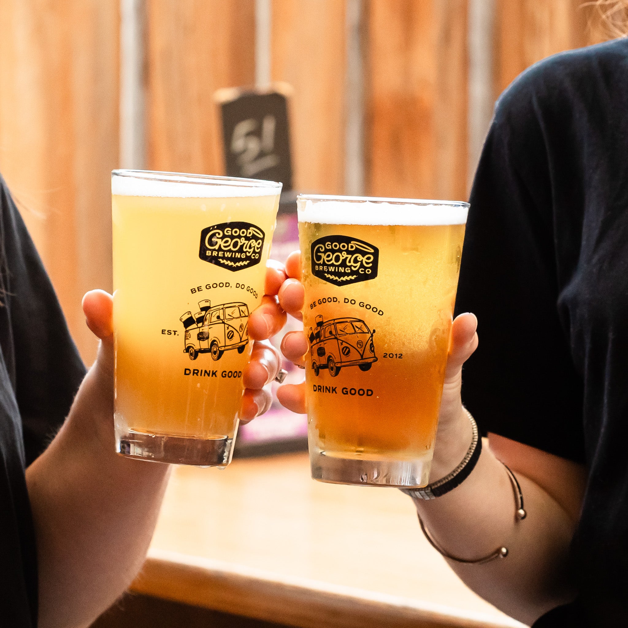 Two glasses of beer from Good George Brewing Co getting cheered together with wooden background