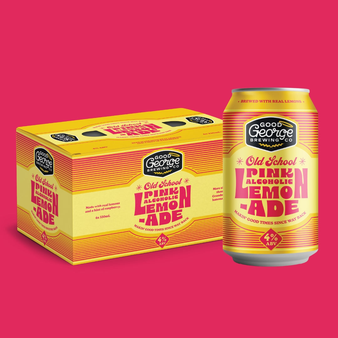 A yellow and orange carton of Good George Brewing Co. Old School Pink Alcoholic Lemonade next to a matching single can of the beverage, set against a solid pink background.