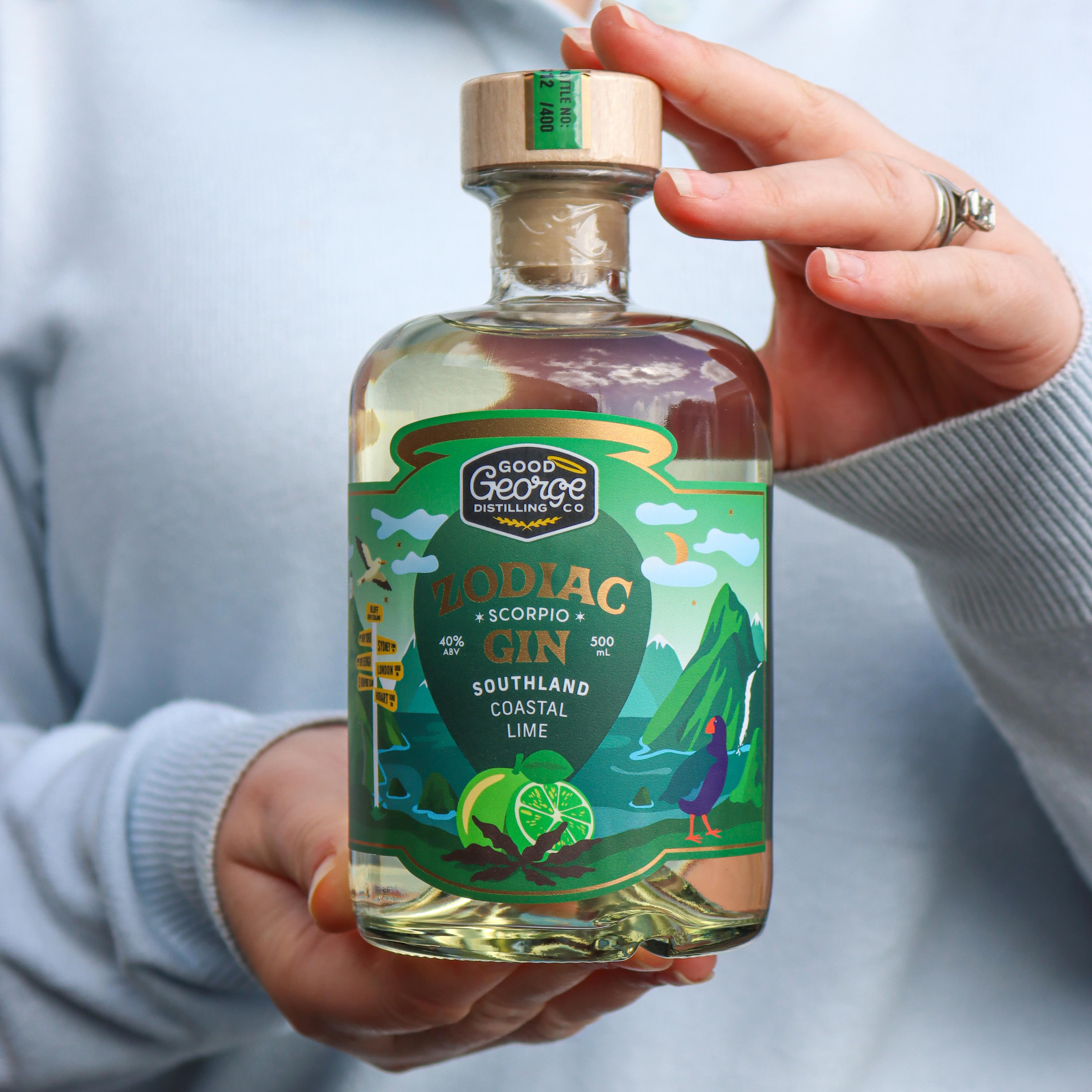 Bottle of Good Good Gin with a colorful label held by a person against a neutral background