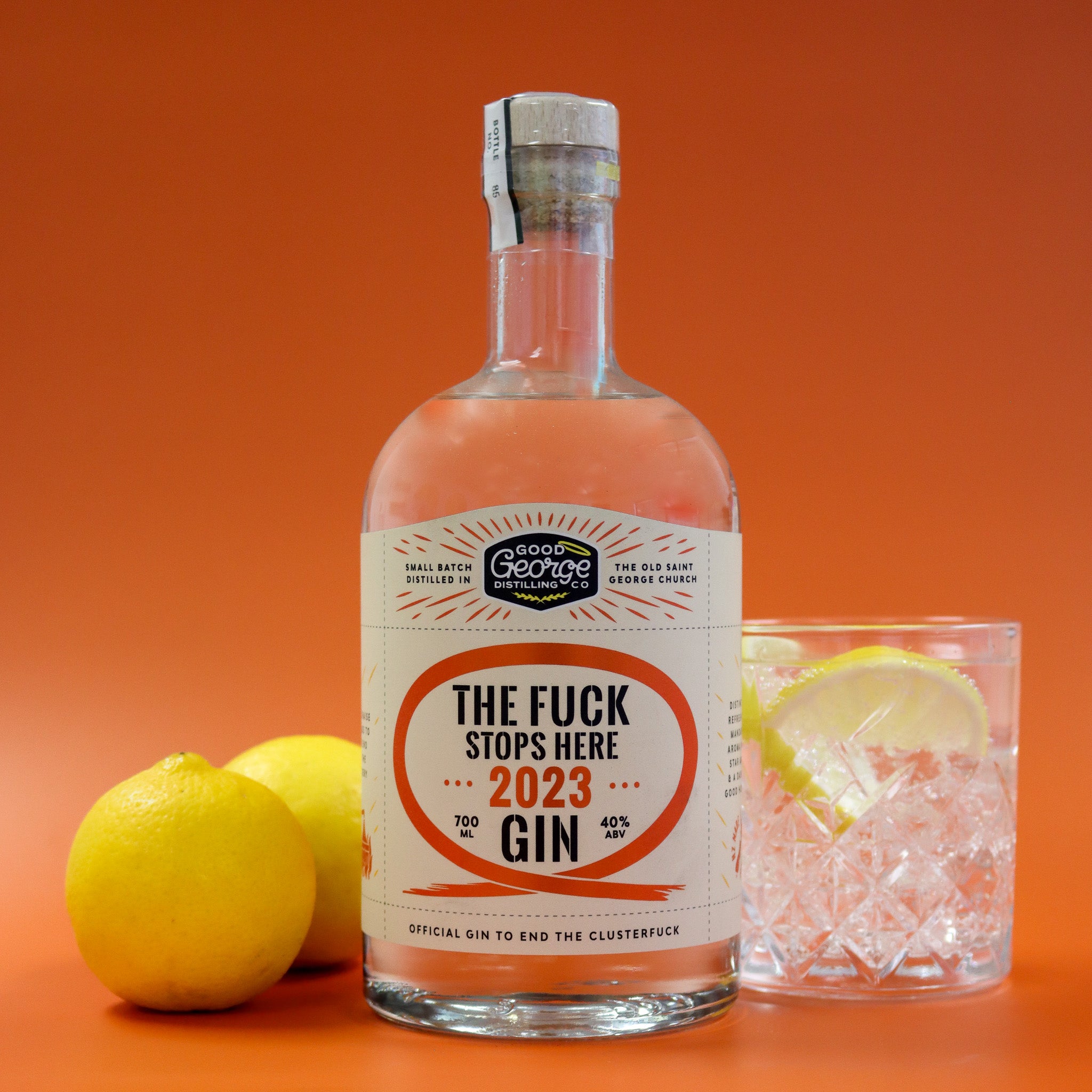 Bottle of gin with a humorous label, lemons, and a glass of gin on an orange background