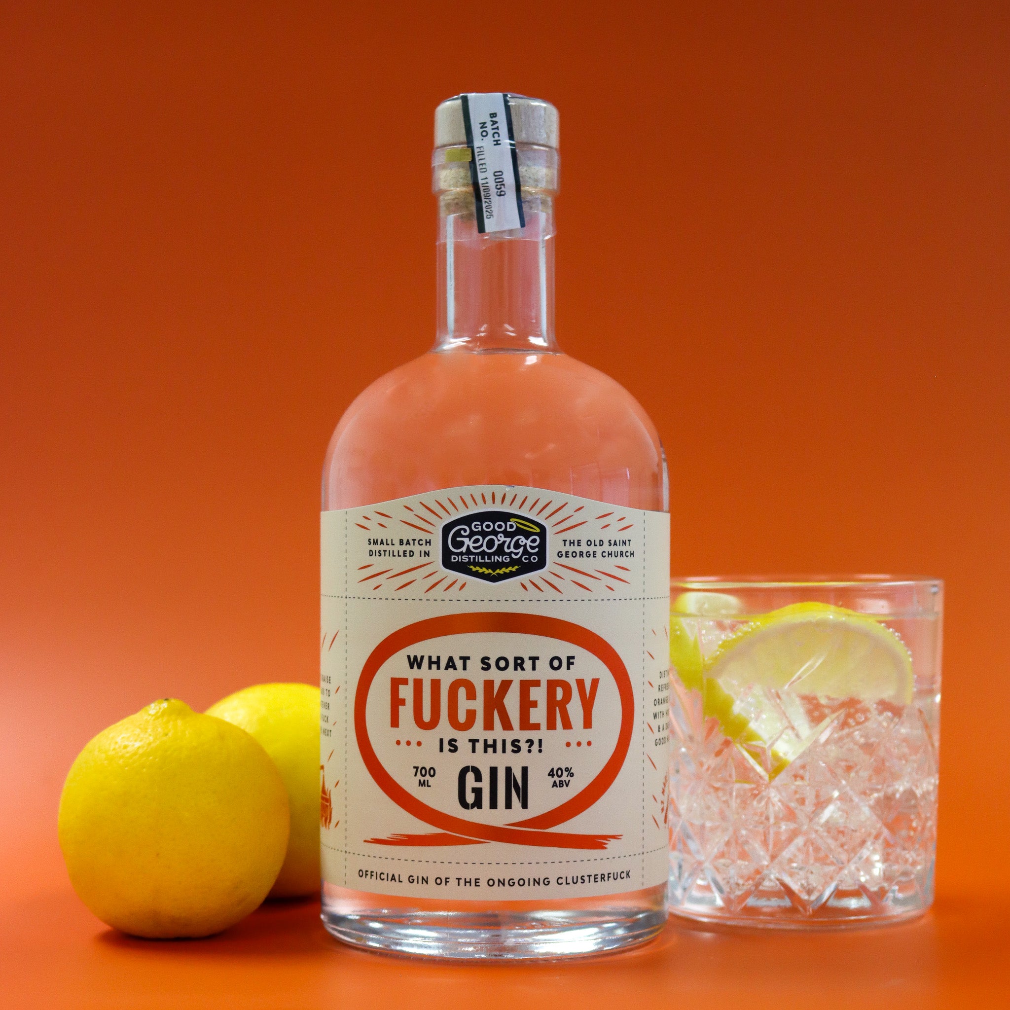 Bottle of gin with a humorous label, lemons, and a glass of gin on an orange background