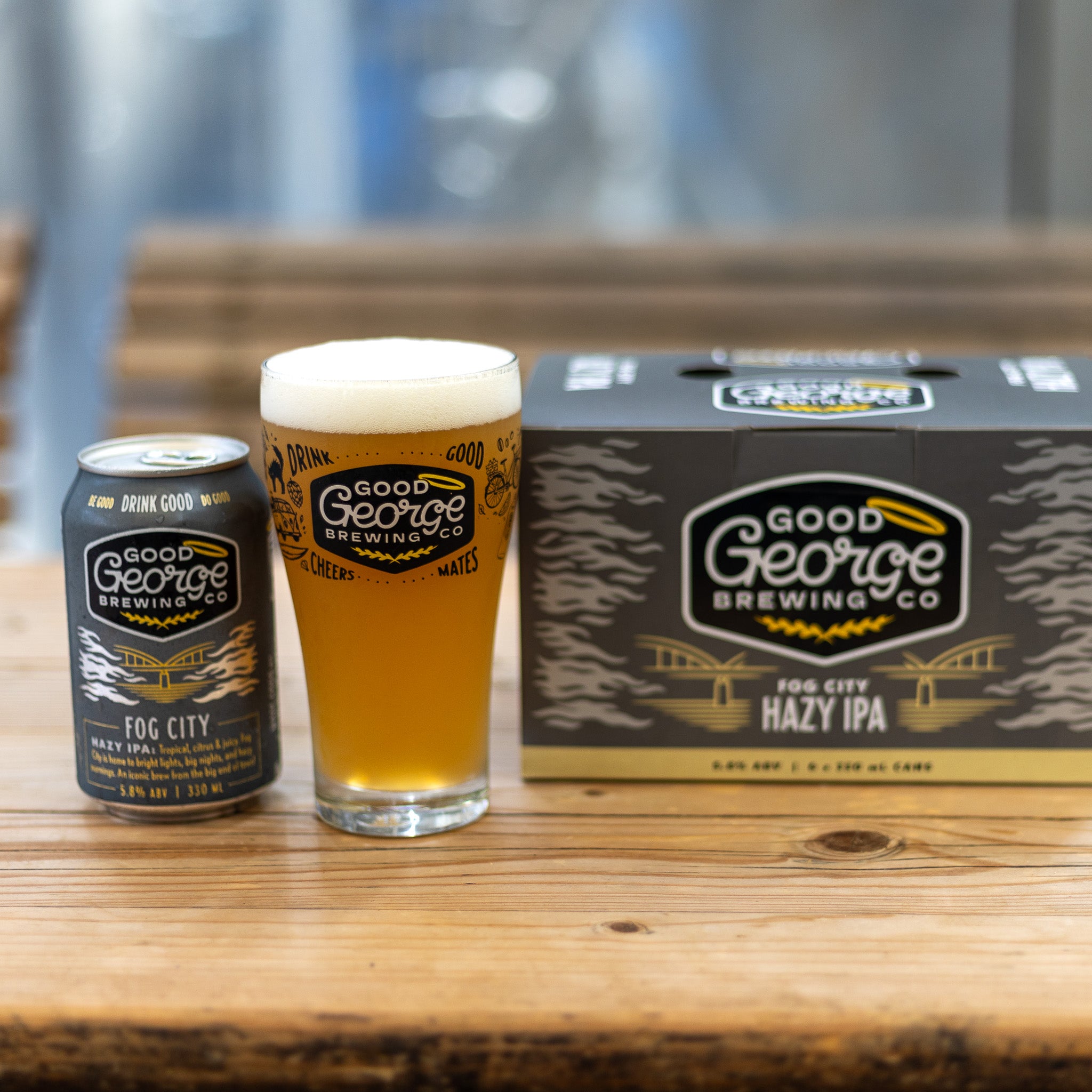 Good George Brewing Co. beer can, glass, and six-pack on a wooden surface.