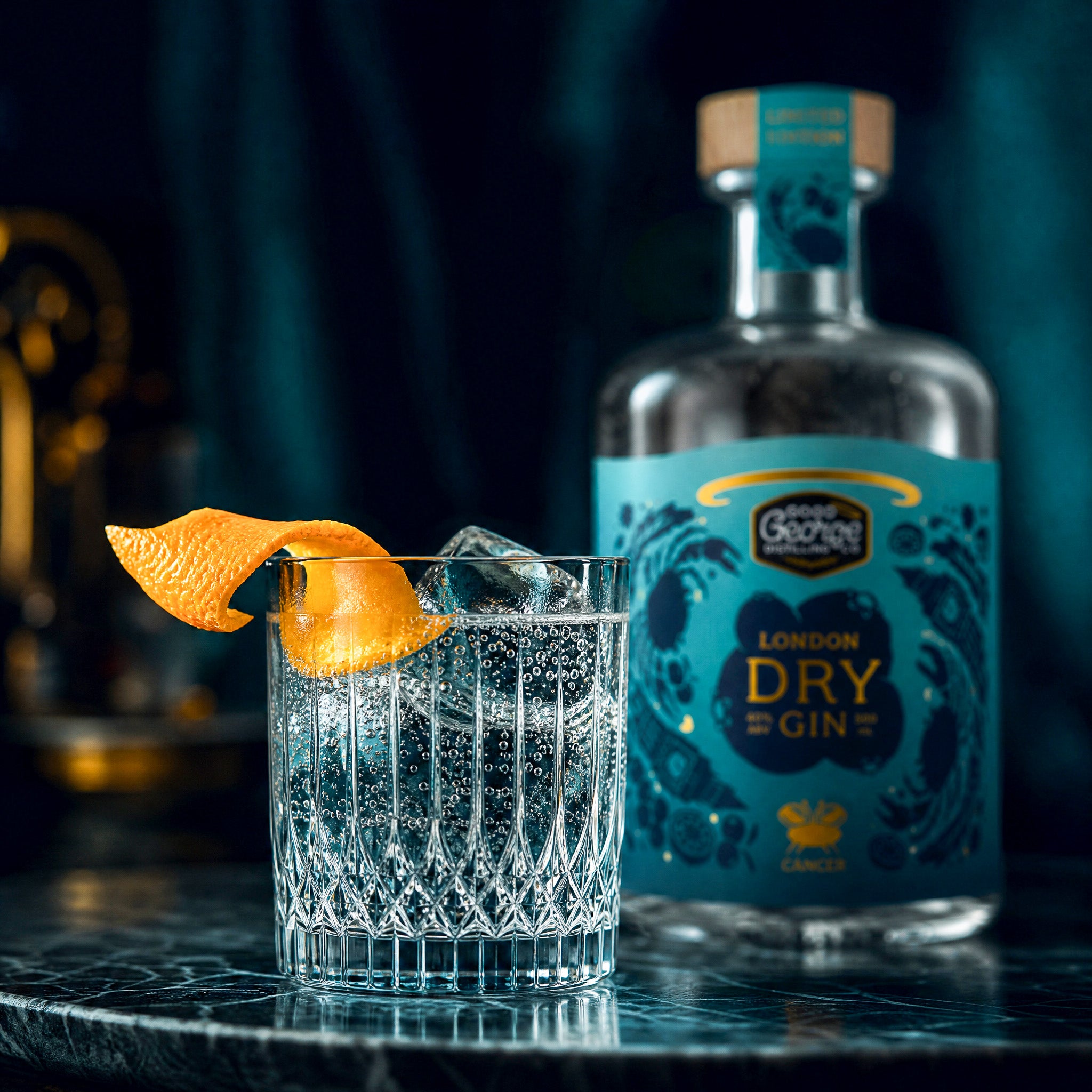 Glass of gin with tonic and orange peel next to a bottle of Good George London Dry Gin on a dark surface.