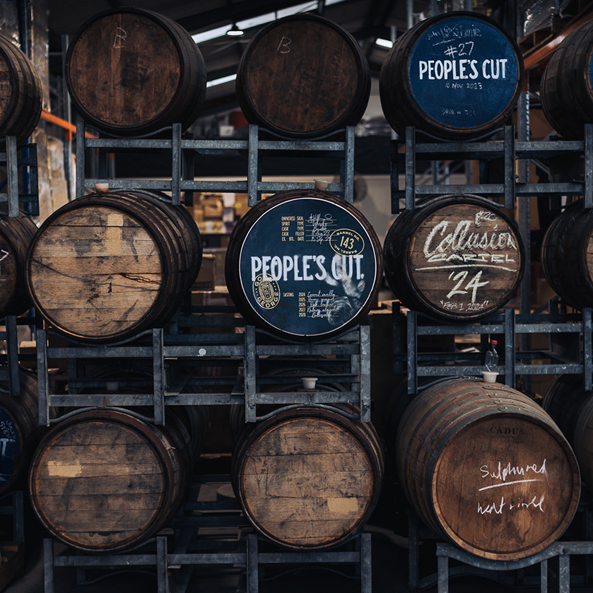 Stacks of wooden barrels with 'People's Cut' branding in a warehouse setting.